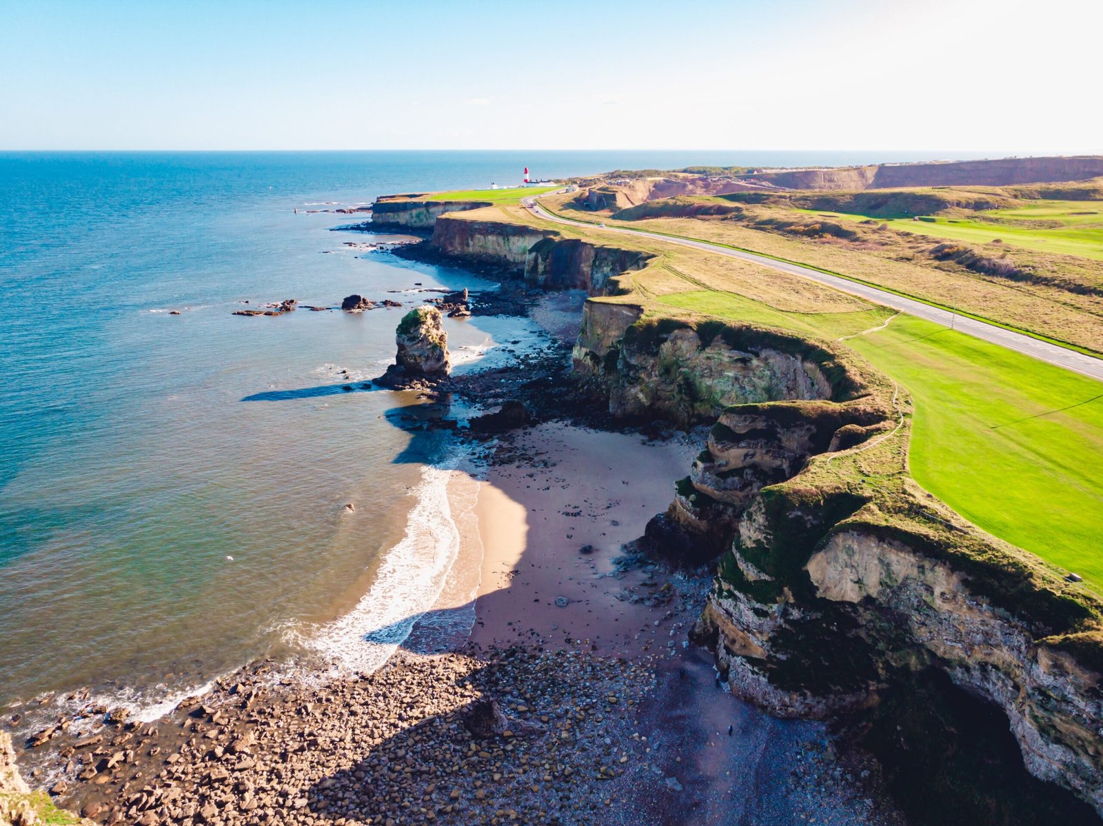 An aerial shot of a clear blue sea and a grassy shore